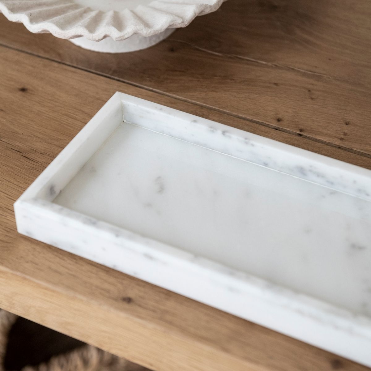 Detalle de bandeja de mármol blanco con vetas grises sobre superficie de madera.
