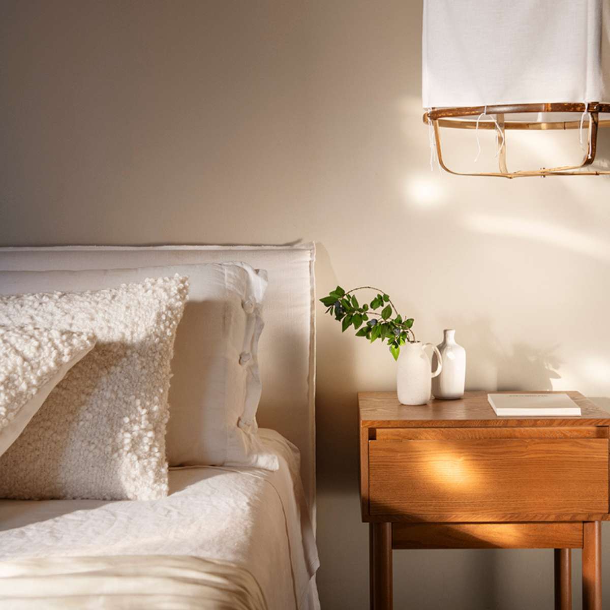 Dormitorio con cama blanca con cojines de bouclé blancos y mesita de noche de madera