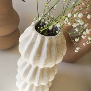 Detalle de jarrón blanco texturizado de diseño ondulado con flores blancas