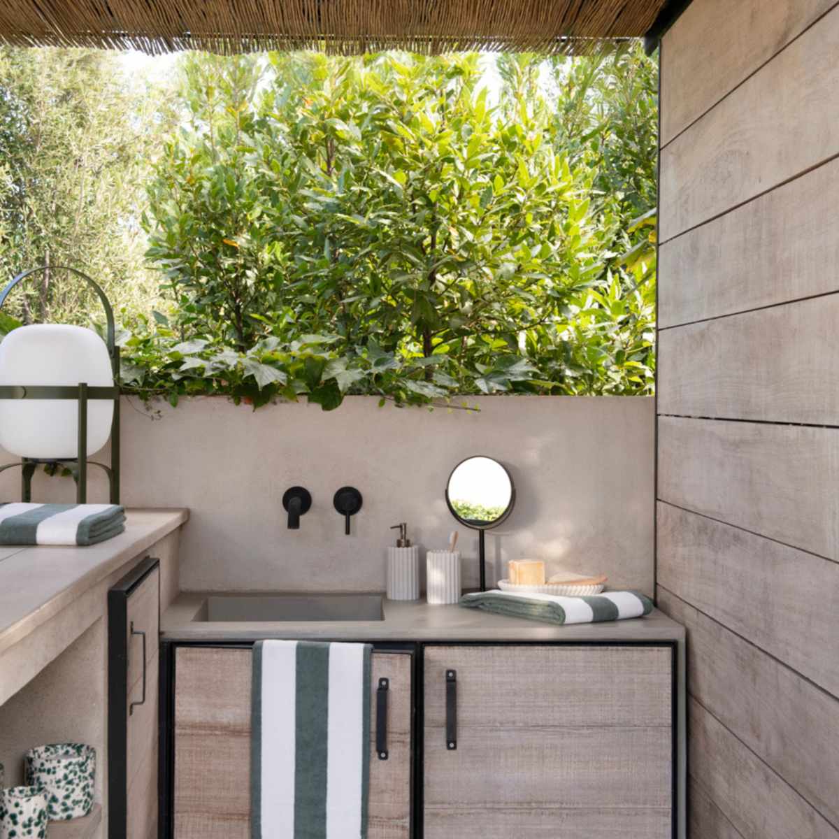 Baño exterior con dispensador de poliresina con rayas beige jarrón decorativo de cerámica y espejo de pie para baño.