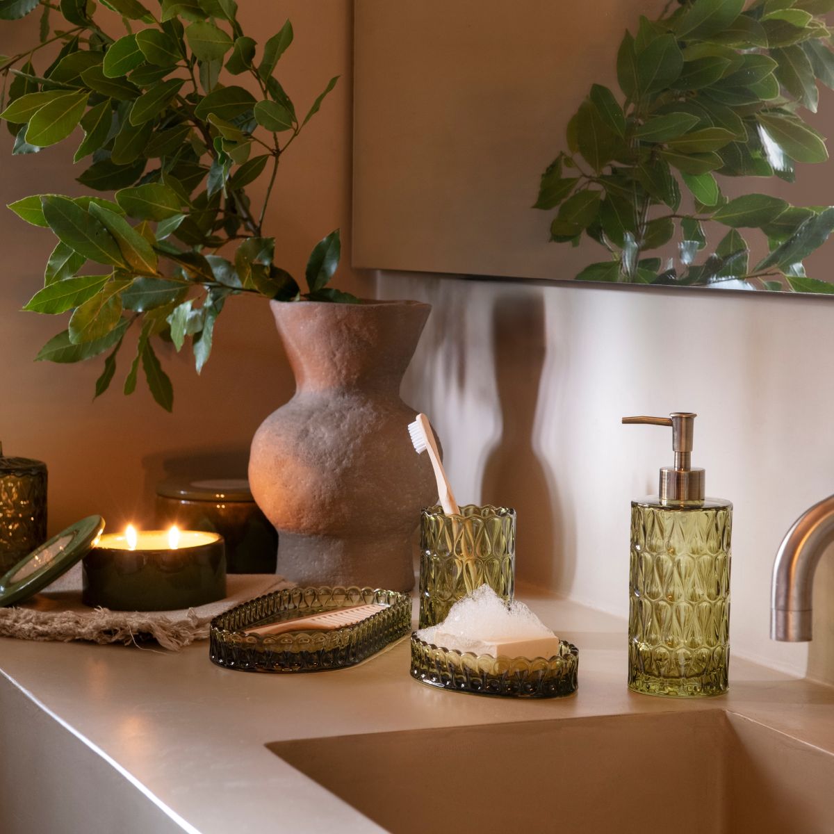 Dispensador de vidrio verde Pear con dosificador bronce en baño con plantas, Andrea House
